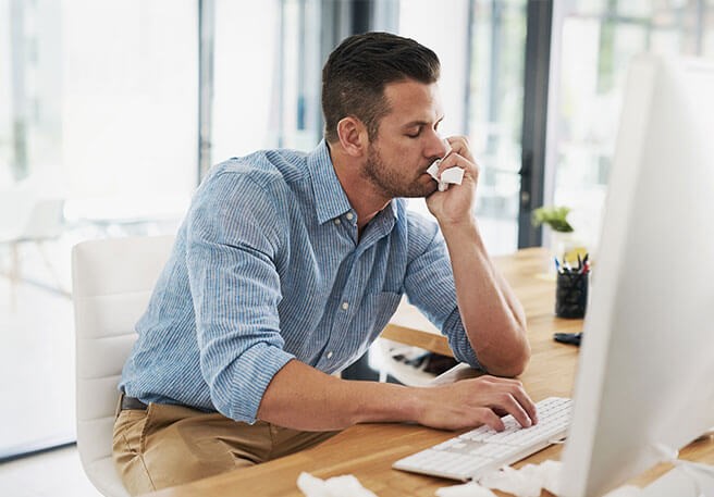 Erkälteter Mann arbeitet am Schreibtisch Arbeiten bei Erkältung
