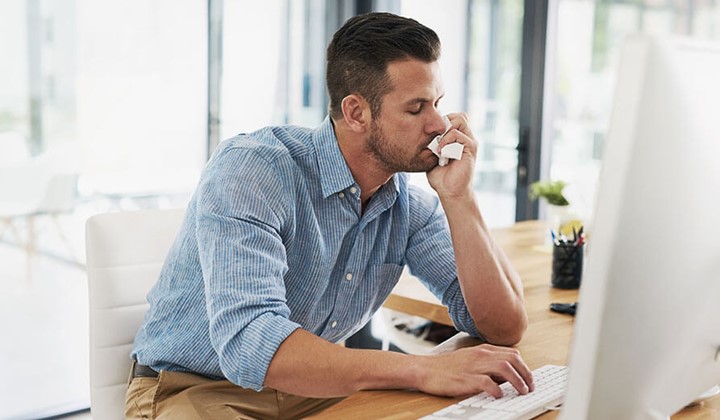 Erkälteter Mann arbeitet am Schreibtisch Arbeiten bei Erkältung