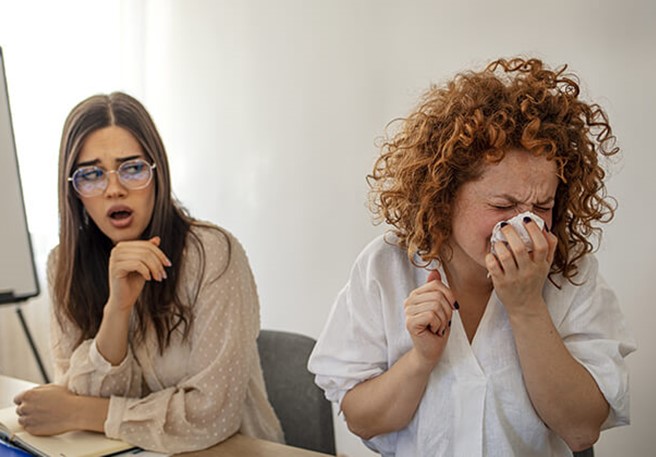 Frau niest im Büro Erkältung ist ansteckend