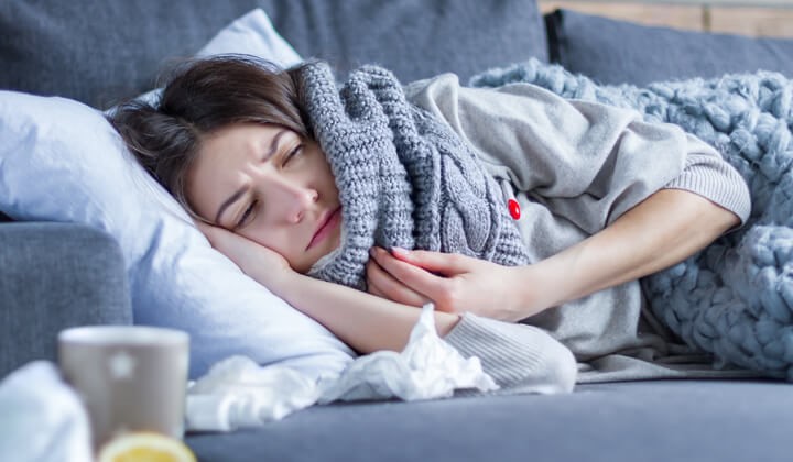 Frau liegt mit Halsschmerzen am Sofa Erkältung mit Halsschmerzen